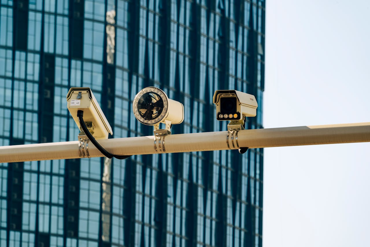 Surveillance cameras mounted on a pole in front of a modern glass building.